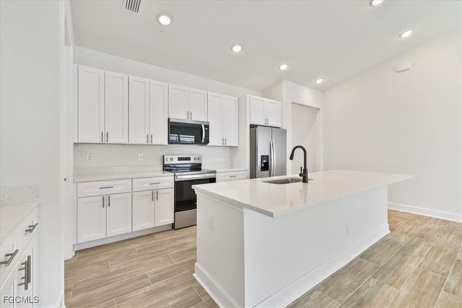 Kitchen featuring appliances with stainless steel finishes, white cabinets, a center island with sink, wood tiled floors, and recessed lighting