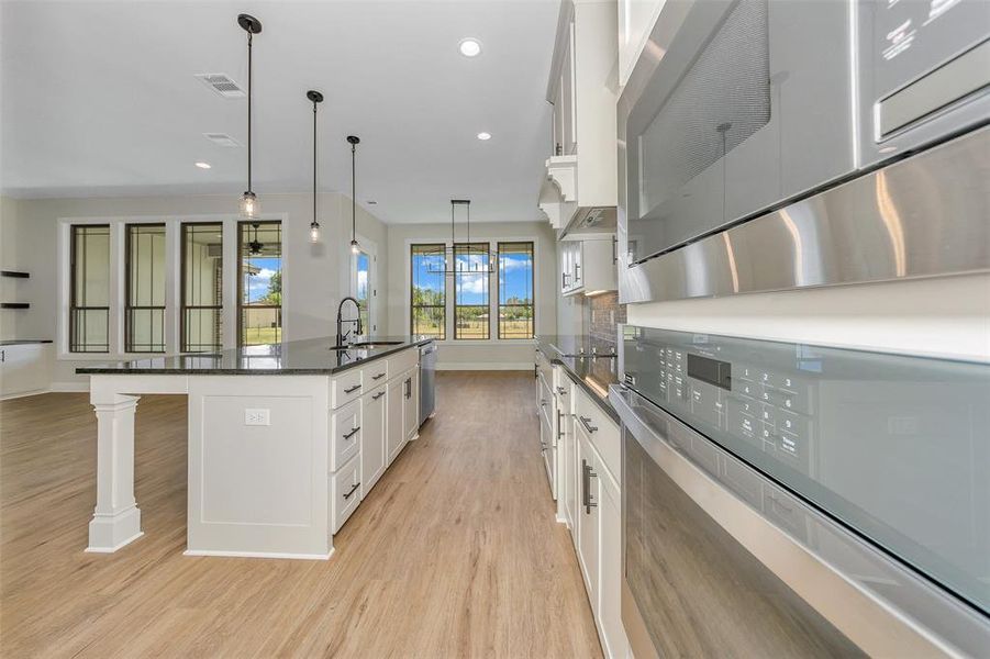 Kitchen with white cabinets, hanging light fixtures, light hardwood / wood-style floors, a center island with sink, and a breakfast bar