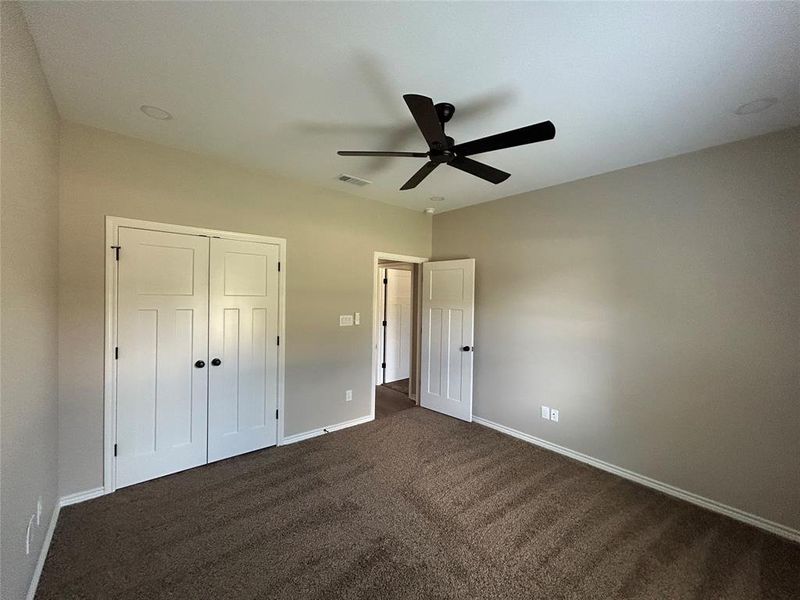Unfurnished bedroom featuring dark carpet, a closet, and a ceiling fan