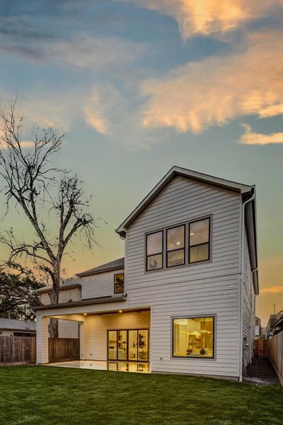 Expansive backyard with lush green lawn and mature trees providing natural shade. A covered patio extends the living area outdoors, ideal for dining and entertaining.