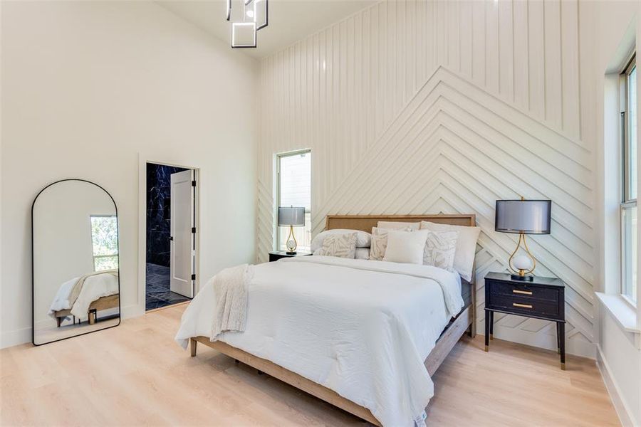 Bedroom with multiple windows, a high ceiling, light wood-style floors, and ensuite bathroom
