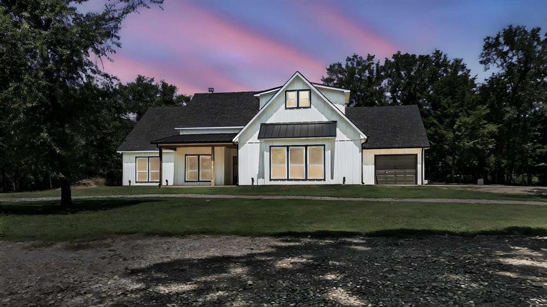 Modern farmhouse with a front lawn, a standing seam roof, roof with shingles, a garage, and a metal roof Modern farmhouse with a front lawn, a standing seam roof, roof with shingles, a garage, and a metal roof