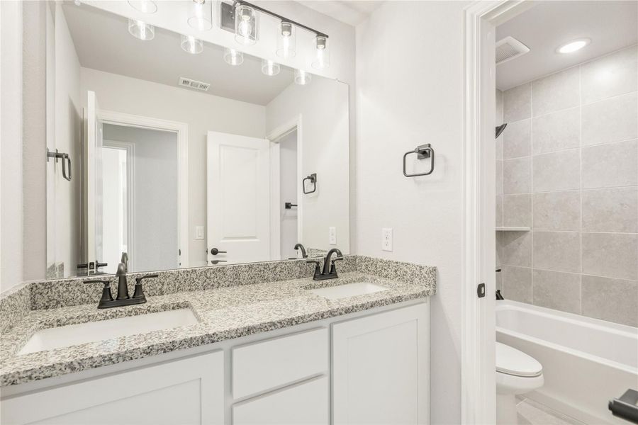 Bathroom with double sink vanity, granite countertop, white cabinets, and tiled shower-tub combo