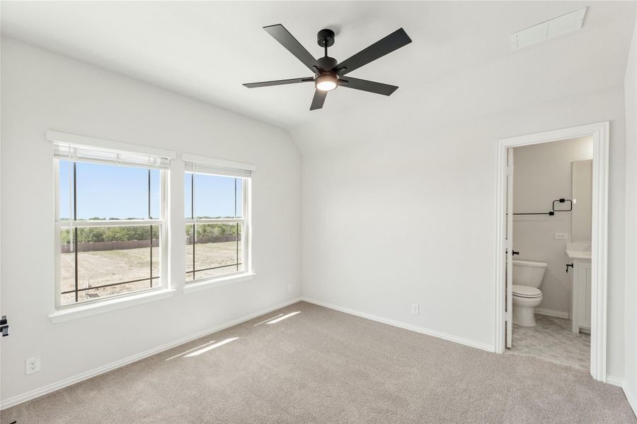 Bedroom with vaulted ceiling, black ceiling fan, carpet flooring, and ensuite bathroom visible through open door