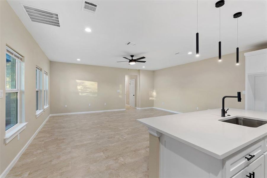 Kitchen featuring white cabinetry, sink, ceiling fan, decorative light fixtures, and a center island with sink