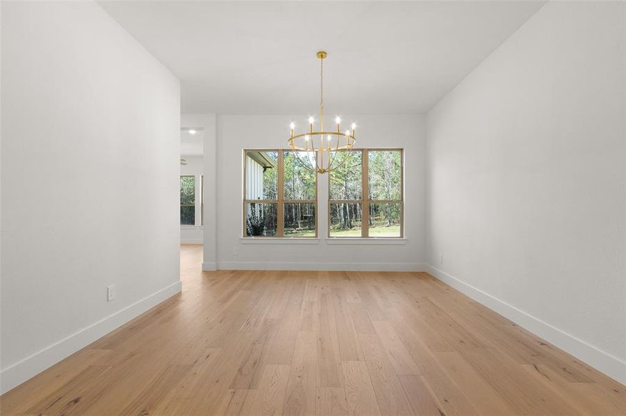 Bright dining room with hardwood floors, a modern chandelier, and large windows offering a view of the outdoors.
