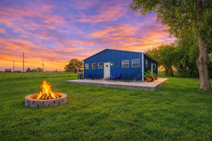 The property features a vibrant blue exterior, a spacious green lawn, and a stone fire pit