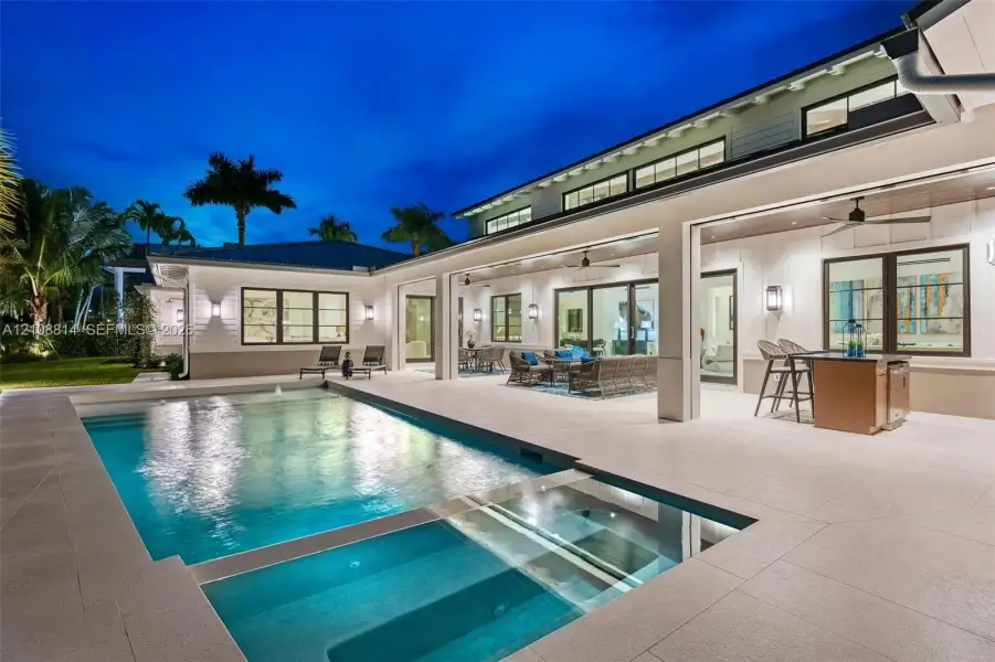 Covered outdoor patio with stone tile flooring, built-in outdoor kitchen, swimming pool with integrated spa, and expansive multi-panel sliding glass doors Covered outdoor patio with stone tile flooring, built-in outdoor kitchen, swimming pool with integrated spa, and expansive multi-panel sliding glass doors