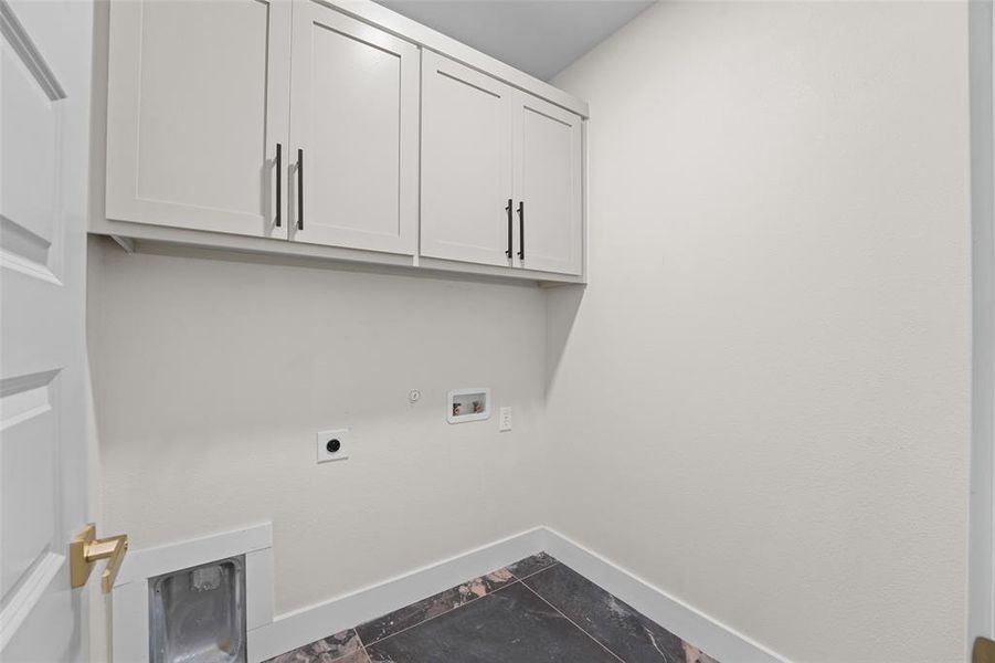 Utility room featuring white shaker cabinetry with black hardware, dark marble-look tile flooring, and white baseboards Utility room featuring white shaker cabinetry with black hardware, dark marble-look tile flooring, and white baseboards