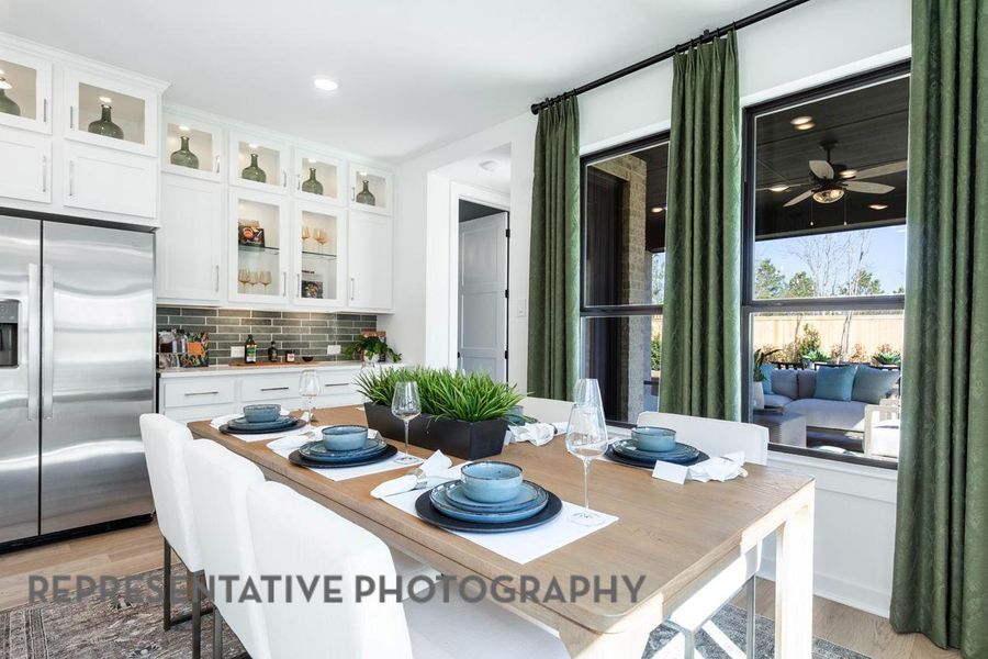 Kitchen featuring stainless steel fridge, tasteful backsplash, light wood-style flooring, glass insert cabinets, and white cabinetry Kitchen featuring stainless steel fridge, tasteful backsplash, light wood-style flooring, glass insert cabinets, and white cabinetry