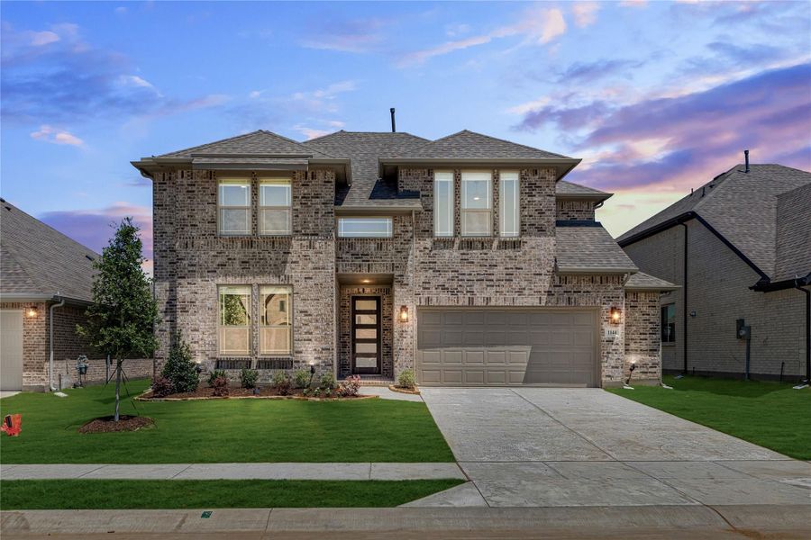 Two-story brick home with two-car garage, modern front door, and manicured lawn at dusk