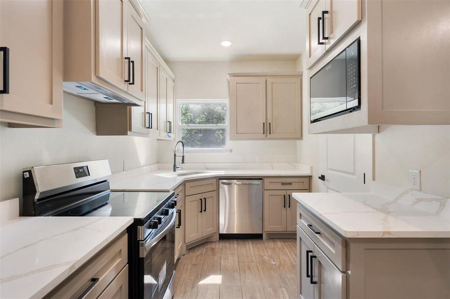 Contemporary kitchen featuring white solid surface countertops, stainless steel appliances, wood-finish flooring, light-toned cabinetry, and black hardware Contemporary kitchen featuring white solid surface countertops, stainless steel appliances, wood-finish flooring, light-toned cabinetry, and black hardware