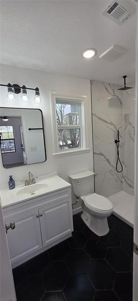 Bathroom with vanity, a marble finish shower, and dark tile patterned floors