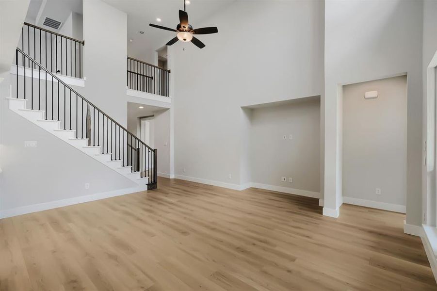 Two-story living area featuring wood-finish flooring, a contemporary staircase with black metal balusters and white risers, a built-in entertainment niche, and a ceiling fan with integrated lighting