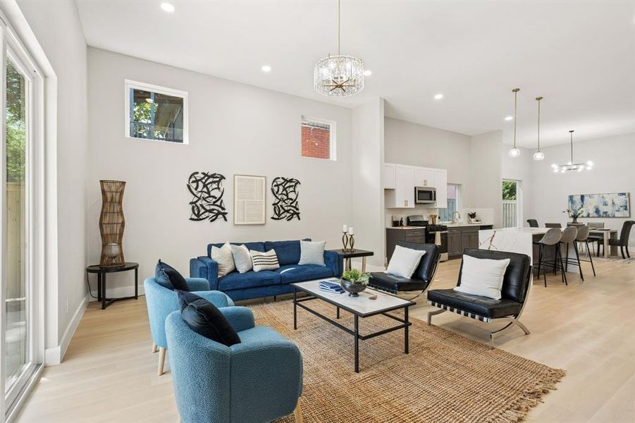 Open-concept living area featuring light wood-finish flooring, recessed lighting, a modern chandelier, and a kitchen with an island Open-concept living area featuring light wood-finish flooring, recessed lighting, a modern chandelier, and a kitchen with an island