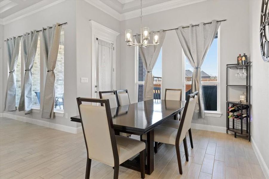 Dining area featuring light wood-type flooring, a notable chandelier, baseboards, and crown molding