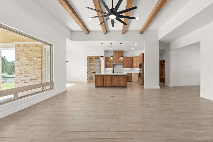 Kitchen with open floor plan, brown cabinetry, a center island with sink, light countertops, and beam ceiling