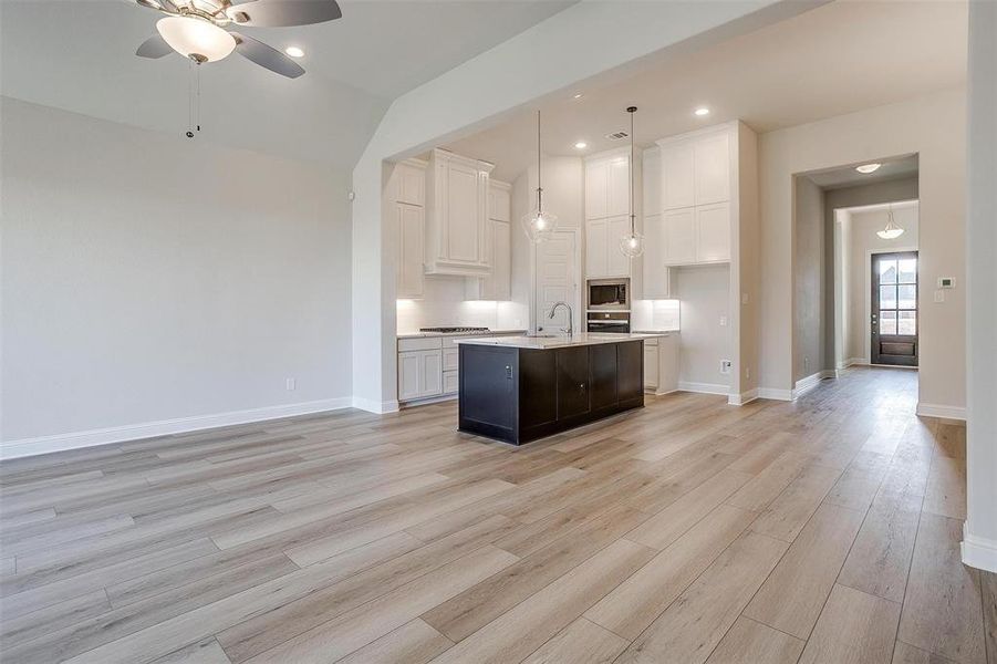 Kitchen featuring appliances with stainless steel finishes, light wood-type flooring, a center island with sink, white cabinetry, and hanging light fixtures