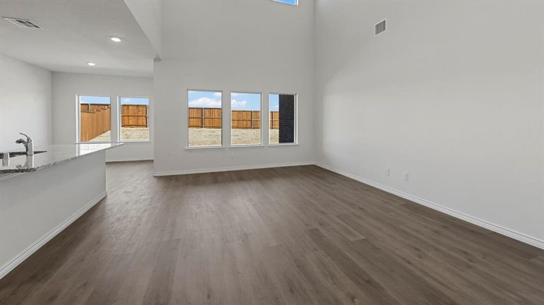 Open-concept living area featuring wood-finish flooring, high ceilings, recessed lighting, and multiple windows providing ample natural light Open-concept living area featuring wood-finish flooring, high ceilings, recessed lighting, and multiple windows providing ample natural light