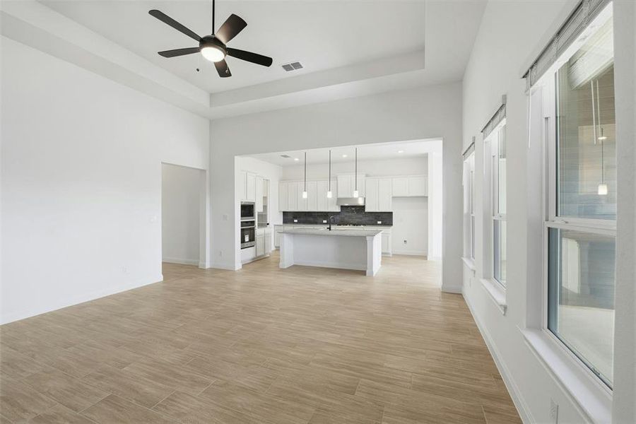 Spacious living area featuring wood-finish tile flooring and a tray ceiling with a black ceiling fan