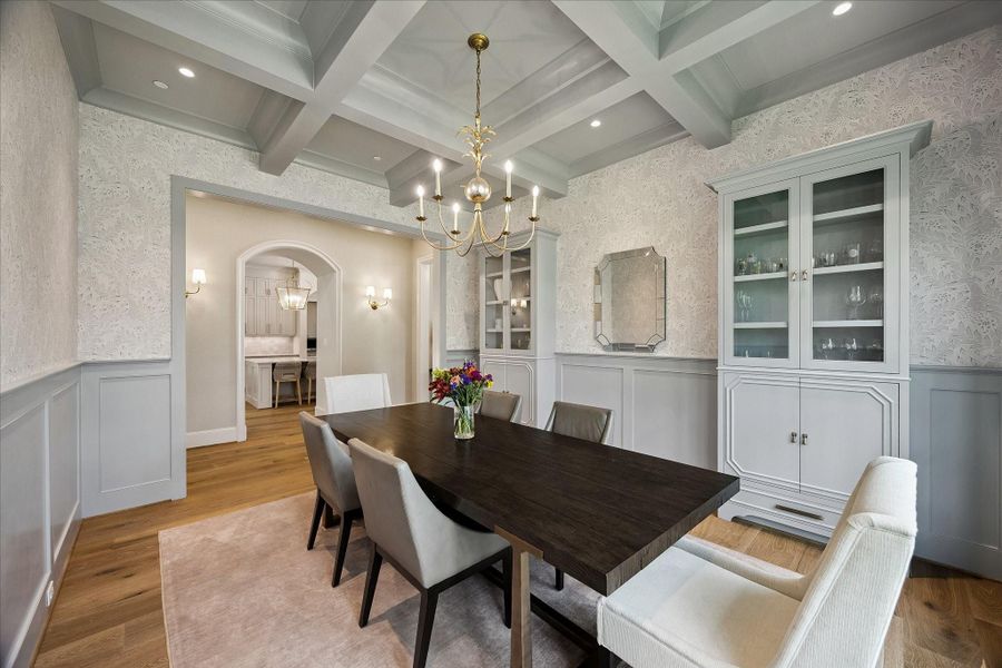 View of dining room toward the kitchen entry showcasing the architectural archway framed with sconce lighting and seamless flow to the kitchen. Designer lighting and tailored millwork enhance the dining room’s elevated design.
