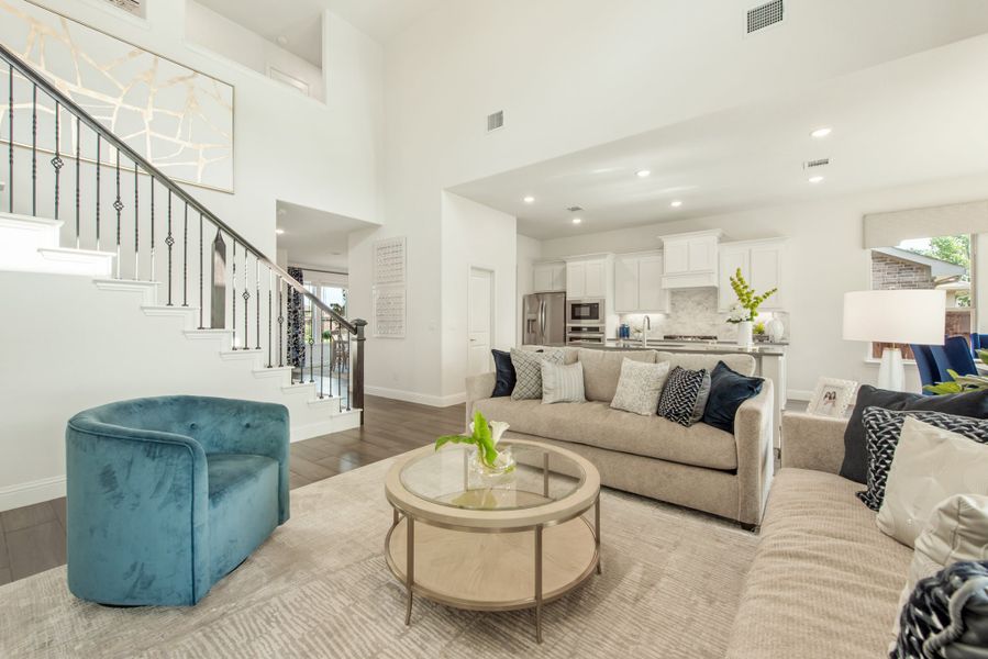 Open-concept living room with high ceilings, staircase, and kitchen visible in background