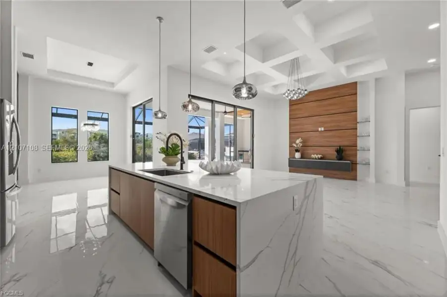 Coffered ceiling, center island with stone-finish waterfall countertop, wood-finish cabinetry, floor-to-ceiling accent wall, and polished tile flooring