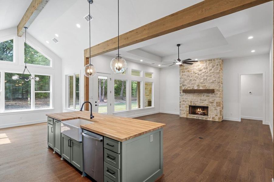 Kitchen with butcher block counters, beam ceiling, pendant lighting, a center island with sink, and a stone fireplace Kitchen with butcher block counters, beam ceiling, pendant lighting, a center island with sink, and a stone fireplace