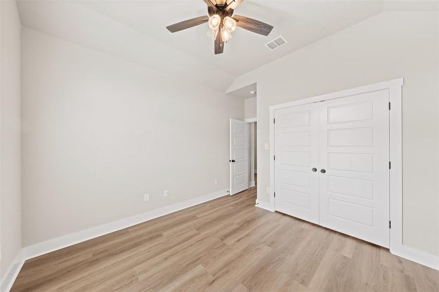 Unfurnished bedroom featuring lofted ceiling, light wood-style floors, a closet, and a ceiling fan
