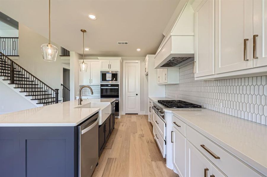 Kitchen featuring backsplash, light hardwood / wood-style flooring, decorative light fixtures, white cabinetry, and stainless steel appliances