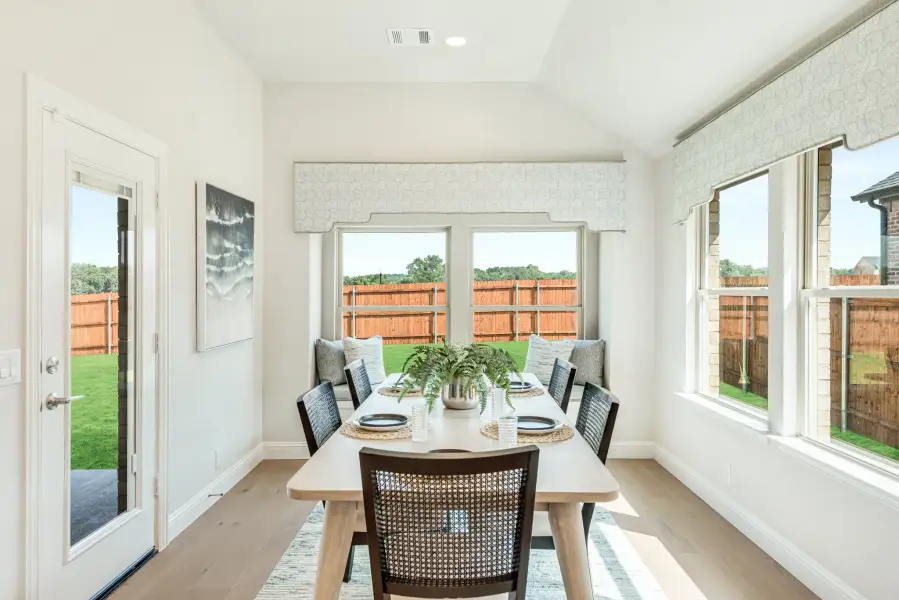 Bright dining nook with vaulted ceiling, large windows, wood table, and built-in bench seating