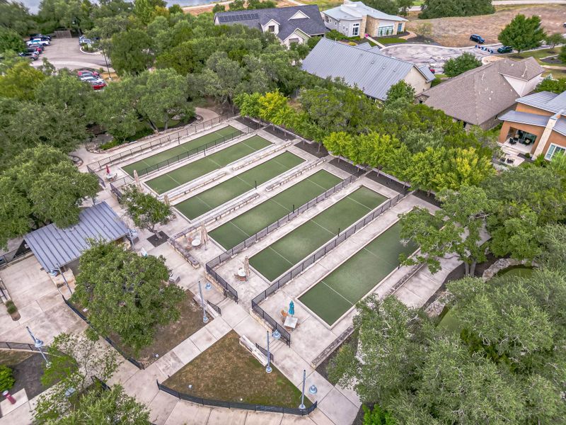 An aerial view reveals multiple bocce ball courts nestled amidst mature trees and a residential community. An aerial view reveals multiple bocce ball courts nestled amidst mature trees and a residential community.
