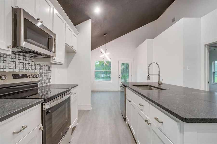 Kitchen featuring appliances with stainless steel finishes, tasteful backsplash, light wood finished floors, white cabinets, and a center island with sink