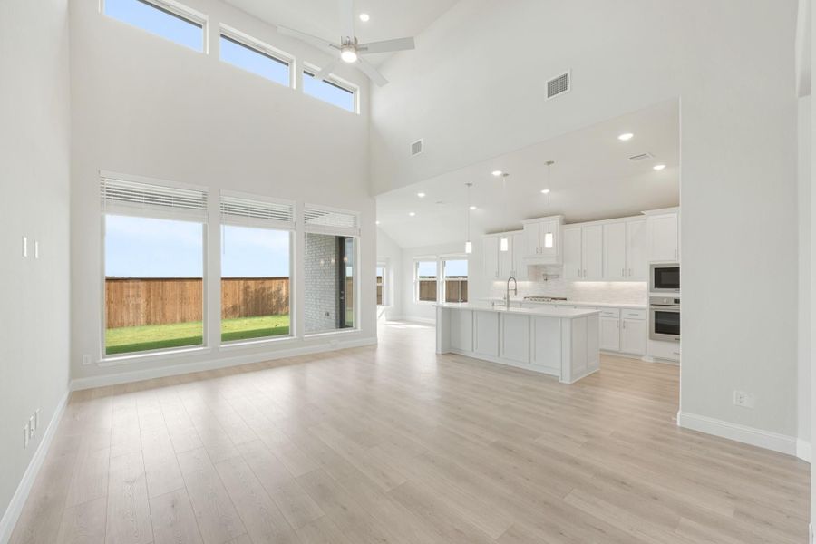 Open living area with two-story ceiling, ceiling fan, and light wood floors flowing into white kitchen with island