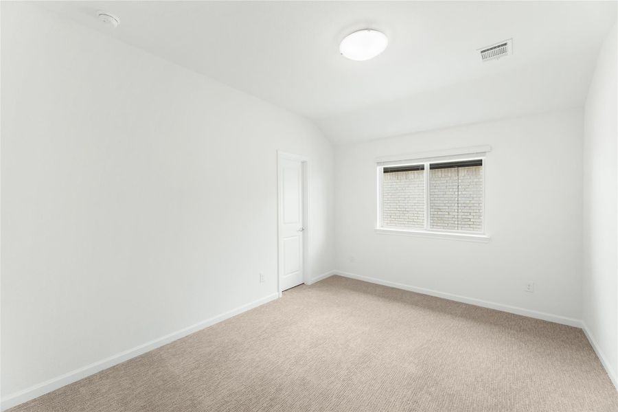 Empty bedroom with white walls, beige carpet, vaulted ceiling, and single window