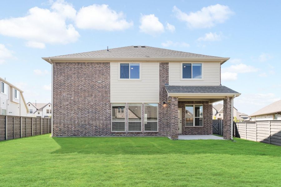 Two-story brick home rear exterior with covered patio, large backyard, and wood privacy fence