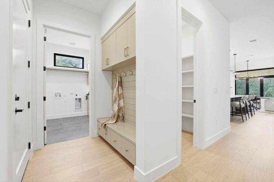 Entryway featuring wood-finish flooring, a built-in mudroom bench with upper cabinetry and storage drawers, and an adjacent utility room with tile flooring and a horizontal window
