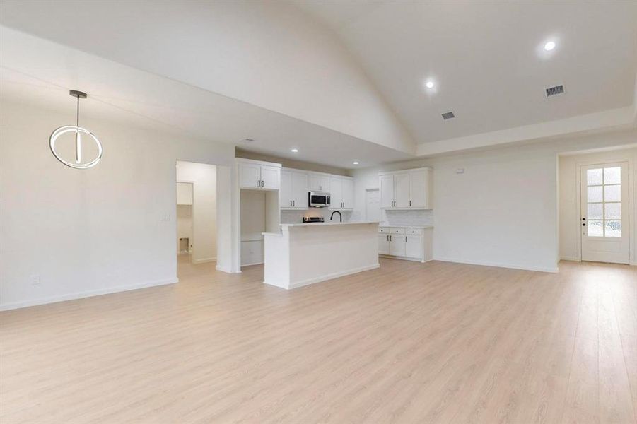 Unfurnished living room featuring light wood finished floors, high vaulted ceiling, and baseboards