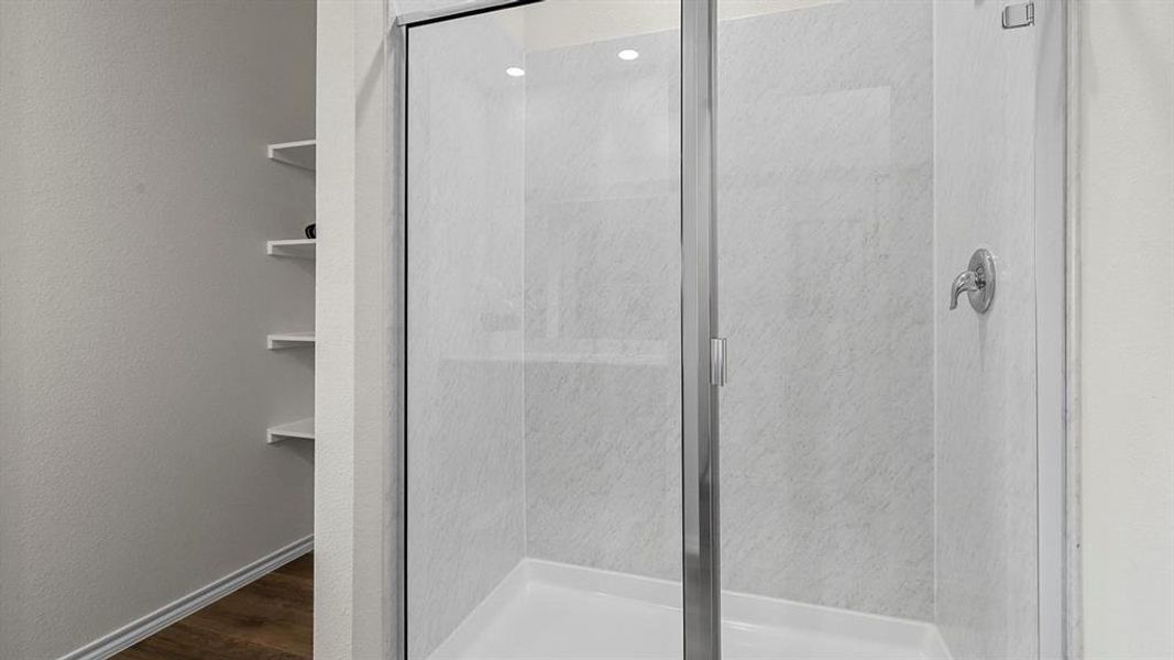 Bathroom with a stall shower, dark wood finished floors, and a textured wall