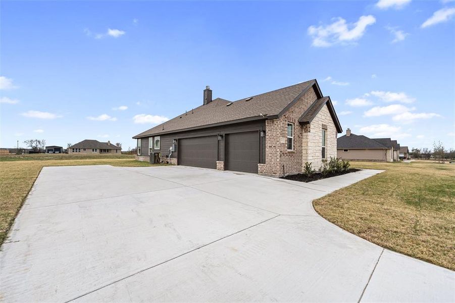 View of side of property with a yard, a shingled roof, a chimney, and driveway