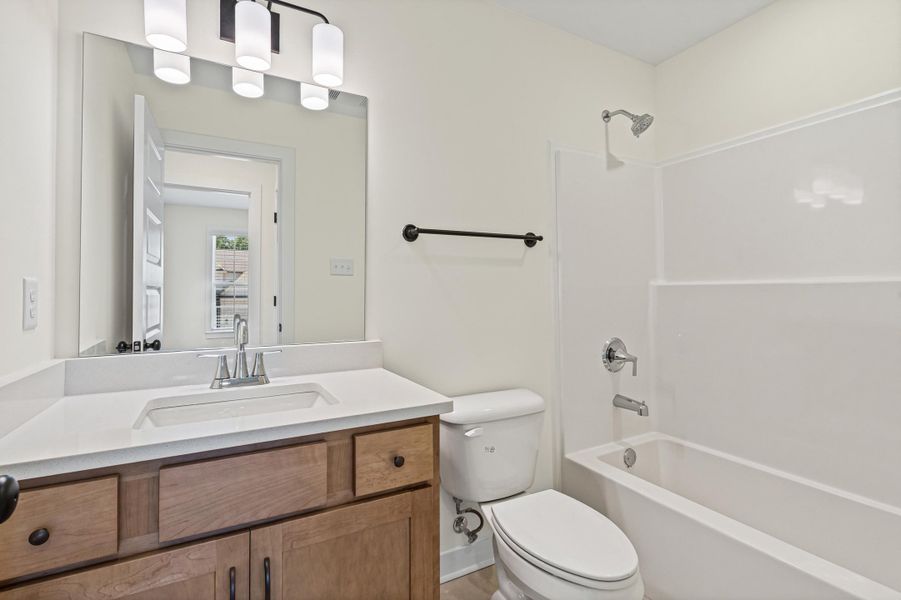 Bathroom featuring a wood-finish vanity with a white countertop and integrated sink, a large wall-mounted mirror, and a contemporary three-light fixture Bathroom featuring a wood-finish vanity with a white countertop and integrated sink, a large wall-mounted mirror, and a contemporary three-light fixture