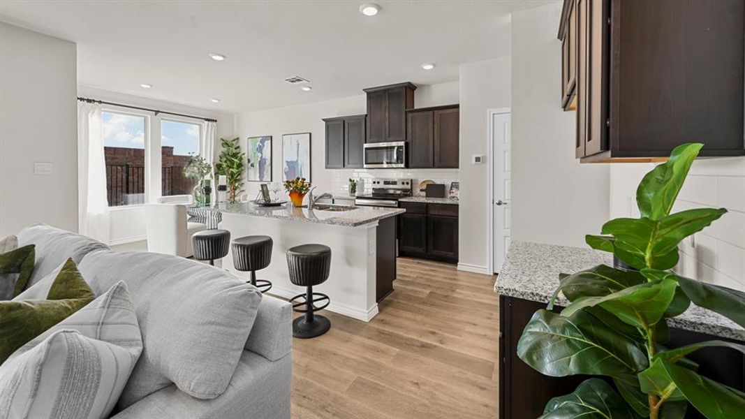 Kitchen featuring open floor plan, light stone counters, tasteful backsplash, an island with sink, and dark brown cabinets