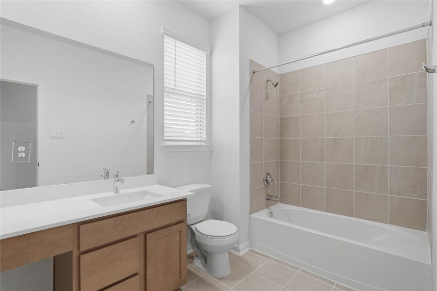 Well-appointed secondary bath with tub/shower combination and tile surround. It also features an extended vanity with a light countertop, a mirror that extends the full length of the vanity, and a window with blinds allowing in the natural light!