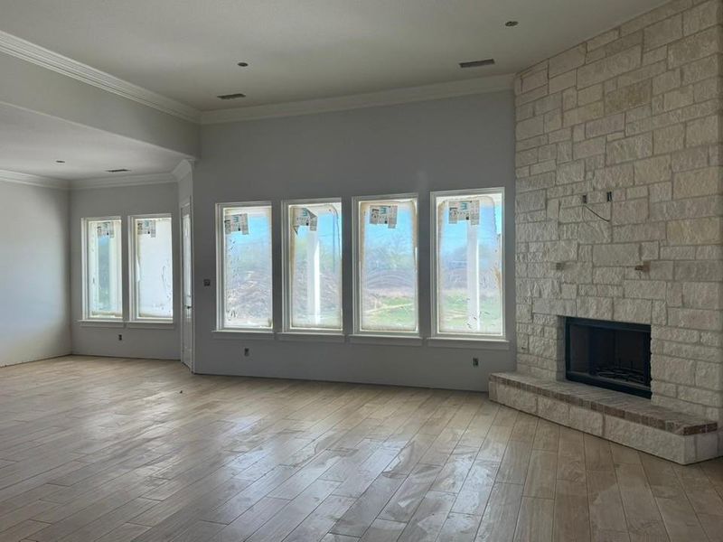 Unfurnished living room featuring a stone fireplace, light wood-style floors, and crown molding