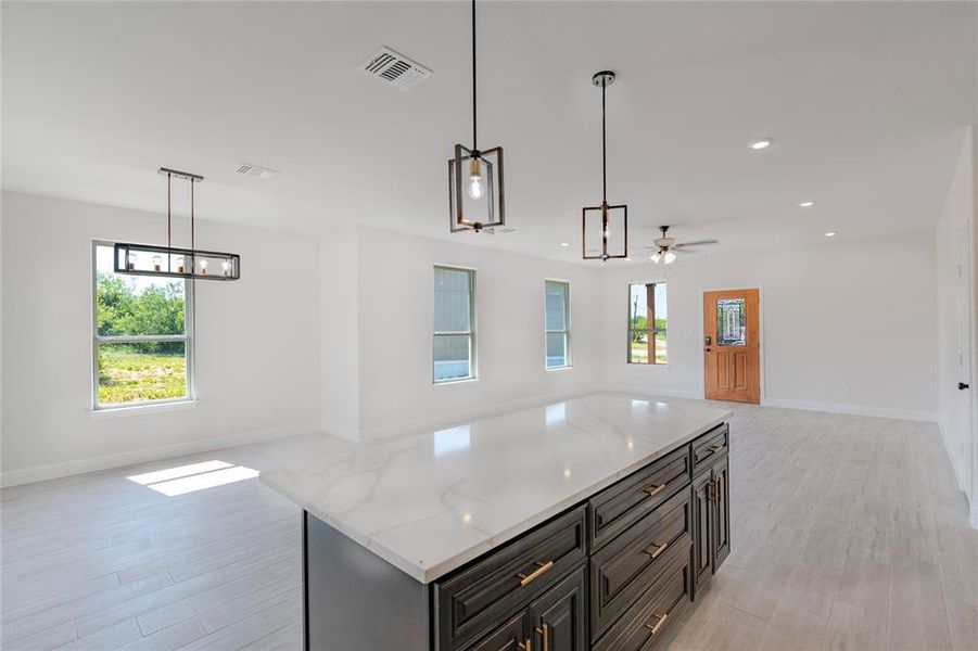 Kitchen with light stone counters, ceiling fan, hanging light fixtures, light hardwood / wood-style floors, and a kitchen island