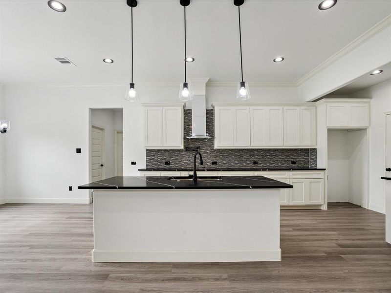 Kitchen featuring light wood-type flooring, white cabinetry, a center island with sink, and decorative backsplash