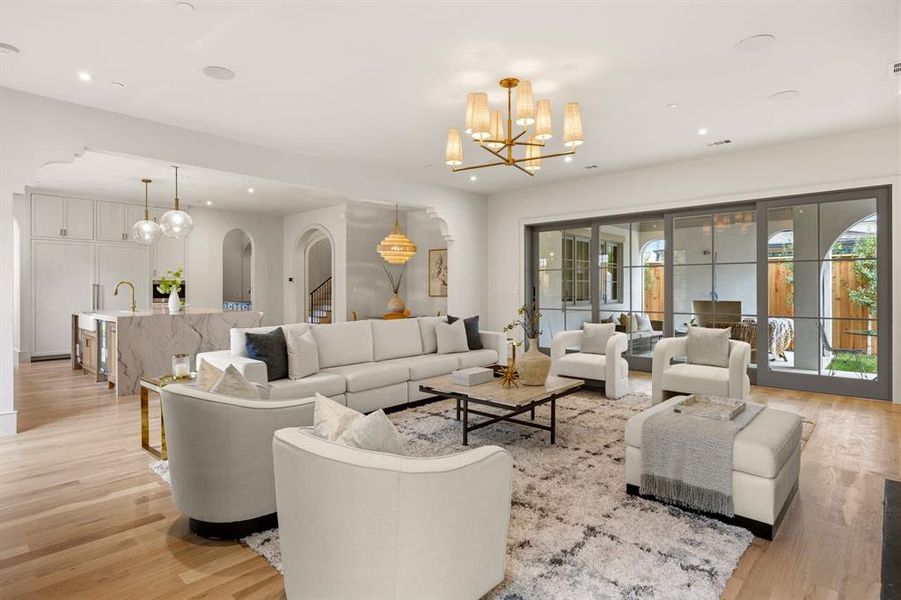 Expansive living space featuring light wood-finish flooring, a contemporary chandelier, and a large multi-panel sliding glass door system Expansive living space featuring light wood-finish flooring, a contemporary chandelier, and a large multi-panel sliding glass door system
