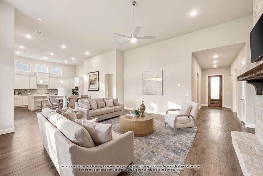 Open-concept living room with high ceilings, stone fireplace, and view into white kitchen with hardwood floors throughout Open-concept living room with high ceilings, stone fireplace, and view into white kitchen with hardwood floors throughout