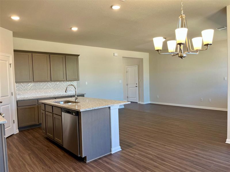Kitchen featuring light stone counters, dark wood-style floors, and an island with sink