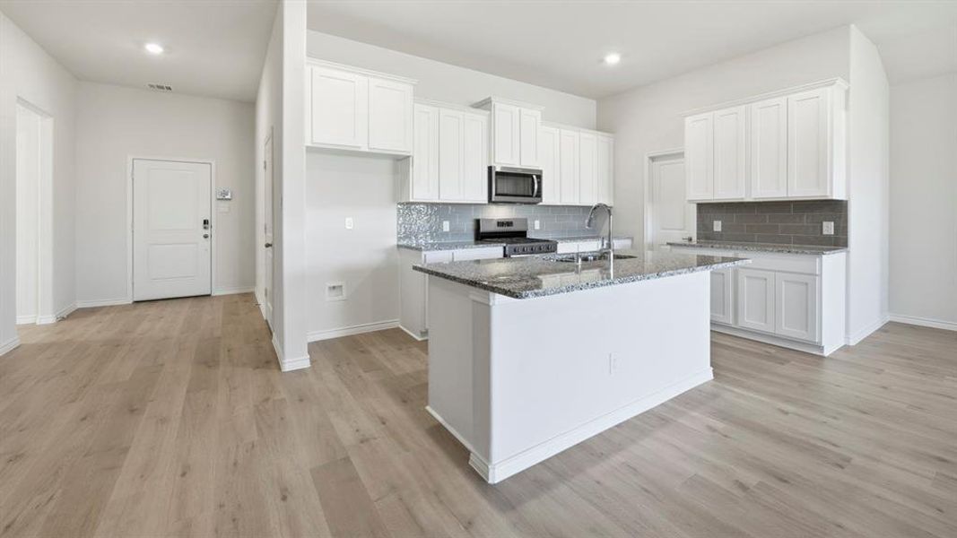 Contemporary kitchen featuring white cabinetry, stainless steel appliances, a center island with a sink, grey subway tile backsplash, and light wood-finish flooring